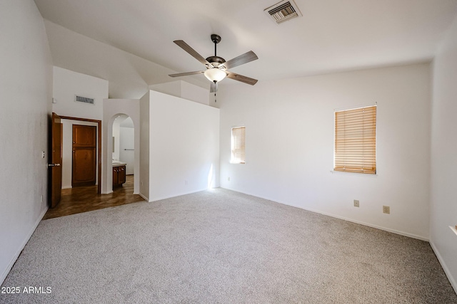 empty room with carpet flooring, arched walkways, visible vents, and ceiling fan