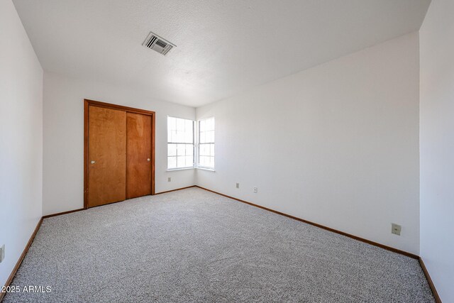 unfurnished bedroom with baseboards, visible vents, a closet, a textured ceiling, and light carpet