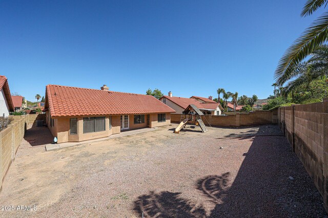 rear view of house with stucco siding, a fenced backyard, a playground, a chimney, and a tiled roof