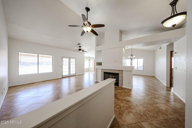 unfurnished living room featuring ceiling fan with notable chandelier, a tile fireplace, baseboards, and vaulted ceiling