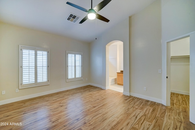 unfurnished bedroom featuring connected bathroom, ceiling fan, light hardwood / wood-style flooring, and a walk in closet