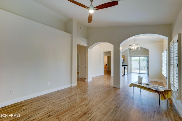 spare room featuring ceiling fan with notable chandelier, lofted ceiling, and light hardwood / wood-style floors