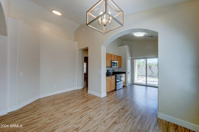 unfurnished living room with an inviting chandelier, light hardwood / wood-style flooring, and lofted ceiling