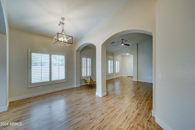 empty room with ceiling fan with notable chandelier and light hardwood / wood-style floors