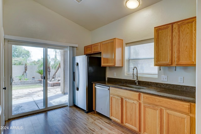 kitchen featuring sink, vaulted ceiling, stainless steel appliances, dark stone counters, and light hardwood / wood-style floors