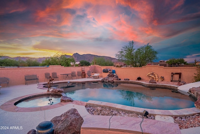 pool at dusk featuring an in ground hot tub, a patio, and a mountain view