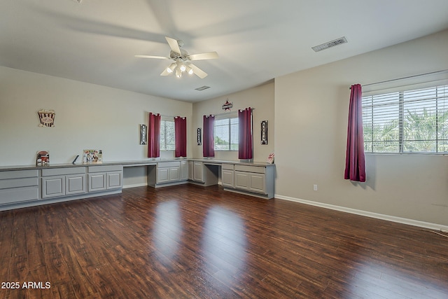 interior space with built in desk, a ceiling fan, baseboards, visible vents, and dark wood-style floors