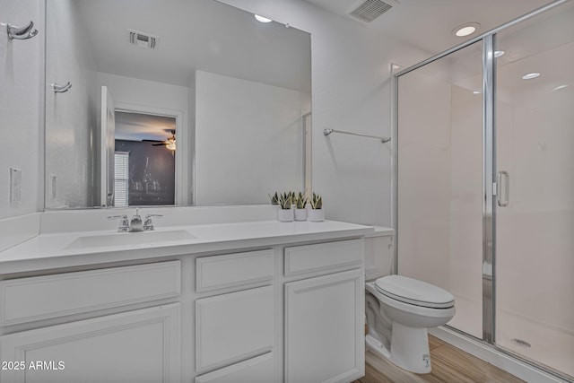 bathroom with hardwood / wood-style flooring, ceiling fan, vanity, toilet, and walk in shower