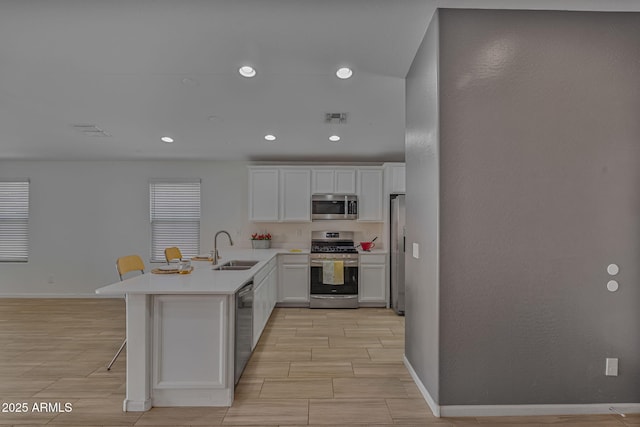 kitchen with sink, a breakfast bar, appliances with stainless steel finishes, white cabinets, and kitchen peninsula