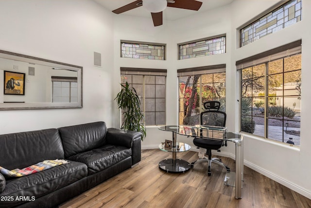 living area with visible vents, a high ceiling, a ceiling fan, wood finished floors, and baseboards