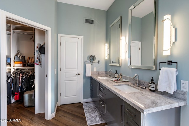 full bath with double vanity, visible vents, a sink, and wood finished floors