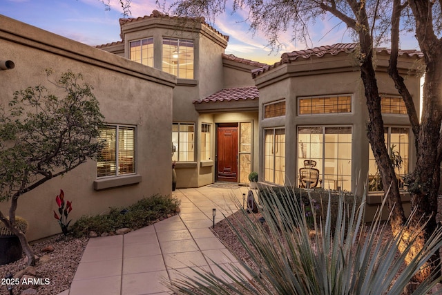 view of front of home featuring stucco siding, a tiled roof, and a patio