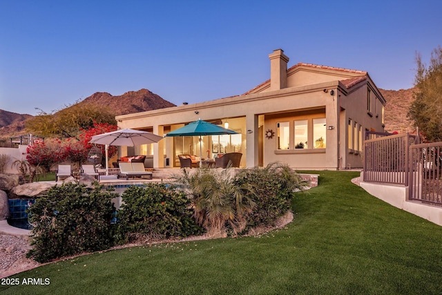 rear view of property with a lawn, a mountain view, a chimney, and stucco siding