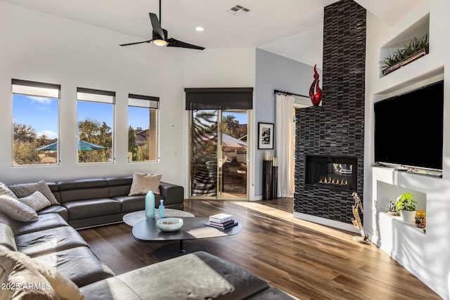 living room featuring visible vents, ceiling fan, wood finished floors, a high ceiling, and a stone fireplace