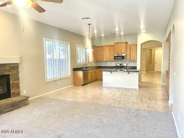 kitchen featuring hanging light fixtures, stainless steel appliances, a center island, light carpet, and a stone fireplace