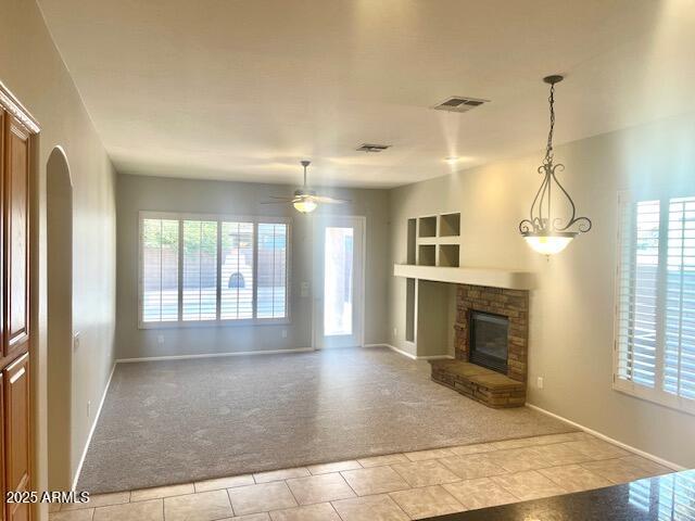 unfurnished living room with light carpet, ceiling fan, a fireplace, and a healthy amount of sunlight