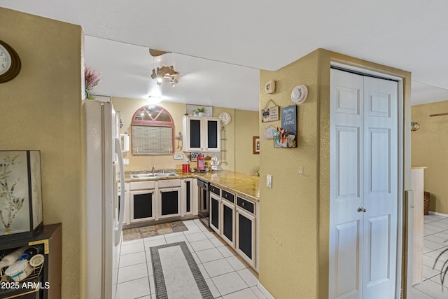 kitchen featuring a peninsula, light tile patterned floors, a sink, and freestanding refrigerator