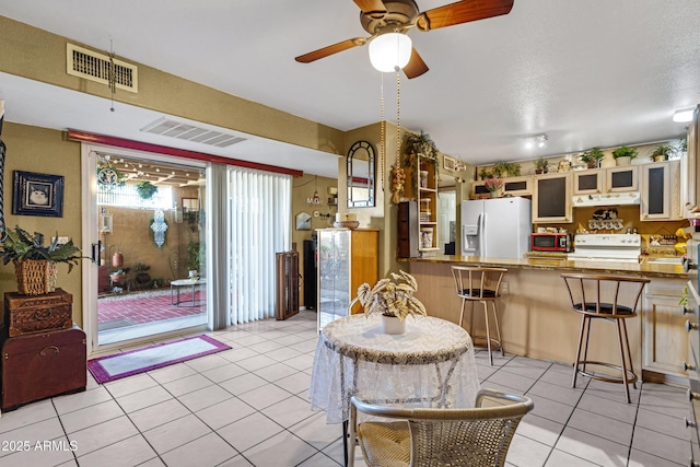 kitchen with visible vents, white refrigerator with ice dispenser, glass insert cabinets, and a kitchen breakfast bar