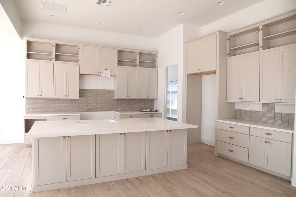 kitchen with decorative backsplash, white cabinets, light hardwood / wood-style flooring, and a kitchen island