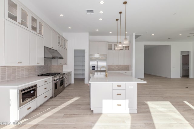 kitchen with white cabinetry, premium appliances, a center island with sink, tasteful backsplash, and decorative light fixtures