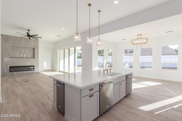 kitchen with decorative light fixtures, a fireplace, light hardwood / wood-style floors, sink, and an island with sink