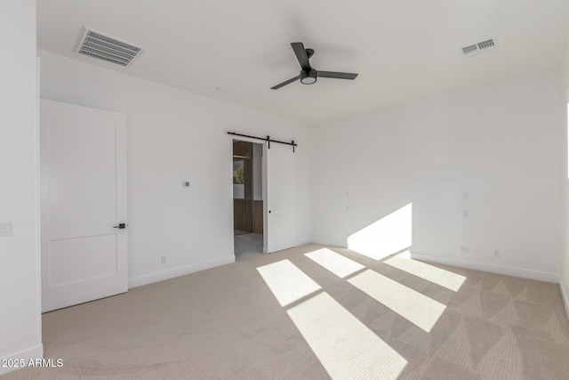 empty room featuring ceiling fan, light carpet, and a barn door