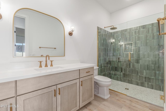 bathroom featuring toilet, vanity, wood-type flooring, and a tile shower