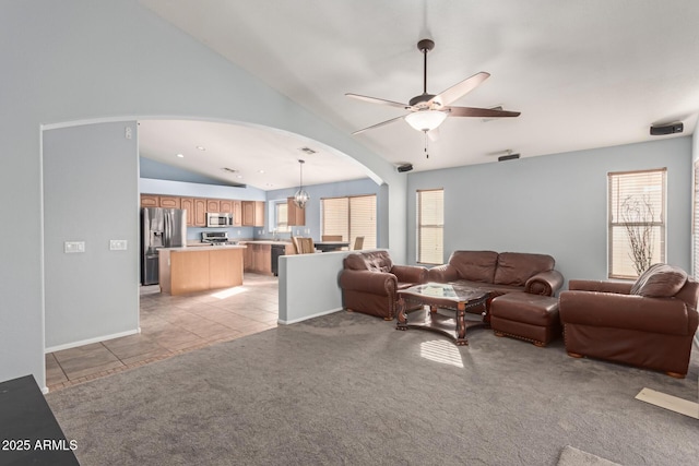 carpeted living room with ceiling fan with notable chandelier, plenty of natural light, and vaulted ceiling