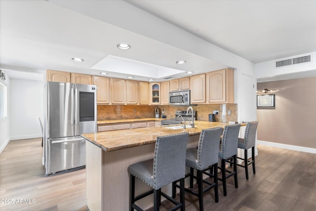 kitchen with a kitchen bar, light brown cabinetry, appliances with stainless steel finishes, kitchen peninsula, and decorative backsplash