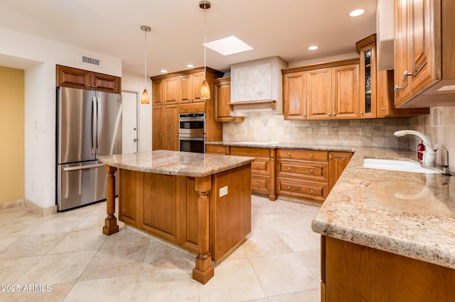 kitchen with sink, light stone counters, a kitchen island, pendant lighting, and stainless steel appliances