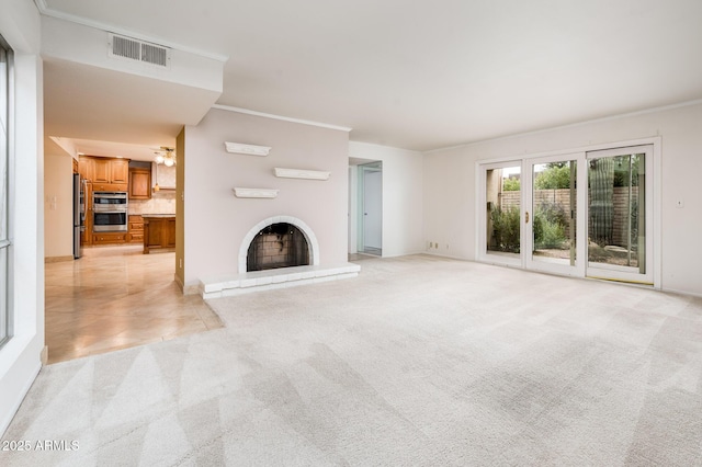 unfurnished living room featuring a brick fireplace, ornamental molding, and light colored carpet