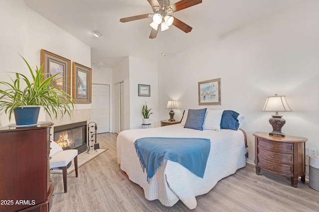 bedroom with a tiled fireplace, a ceiling fan, and light wood finished floors