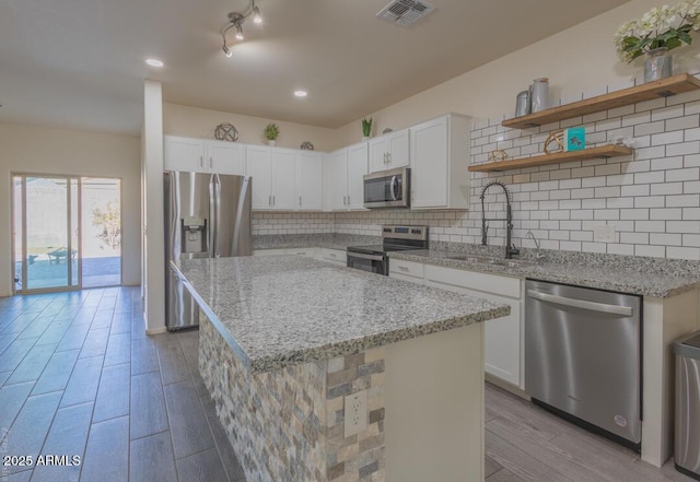 kitchen featuring sink, light stone counters, appliances with stainless steel finishes, a kitchen island, and white cabinets