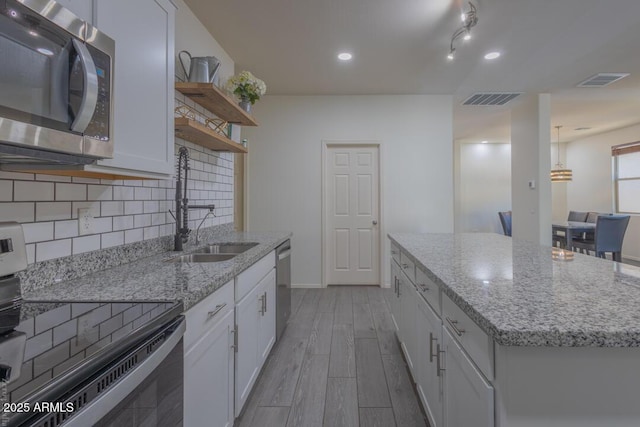 kitchen featuring appliances with stainless steel finishes, tasteful backsplash, white cabinetry, an island with sink, and sink