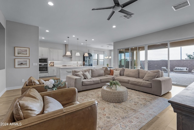 living room featuring sink, light hardwood / wood-style floors, and ceiling fan with notable chandelier