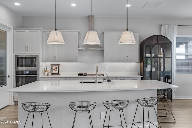 kitchen featuring built in microwave, stainless steel oven, pendant lighting, a kitchen bar, and a kitchen island with sink