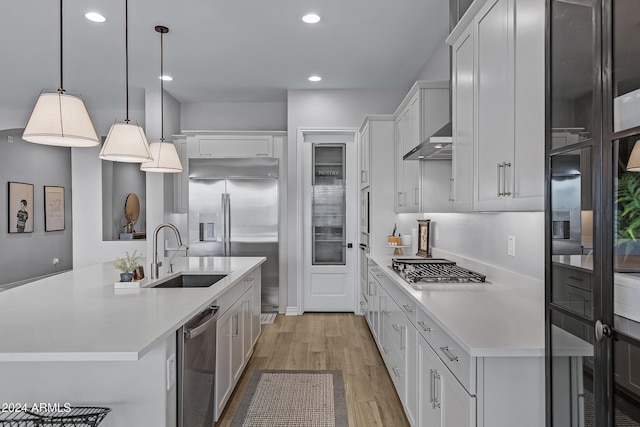 kitchen with a kitchen island with sink, sink, light hardwood / wood-style floors, white cabinetry, and hanging light fixtures