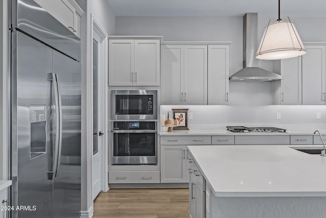 kitchen featuring pendant lighting, white cabinets, sink, built in appliances, and wall chimney exhaust hood