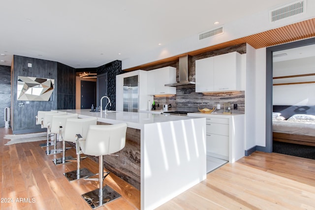 kitchen with wall chimney range hood, stainless steel built in refrigerator, light countertops, a sink, and white cabinets