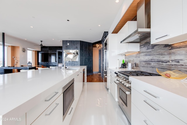 kitchen featuring wall chimney range hood, modern cabinets, appliances with stainless steel finishes, a sink, and white cabinetry