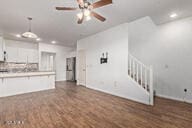 unfurnished living room with dark wood finished floors, stairway, baseboards, and a ceiling fan