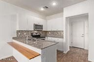 kitchen with visible vents, a peninsula, decorative backsplash, white cabinetry, and stainless steel microwave