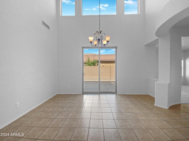 tiled spare room with a chandelier and a towering ceiling