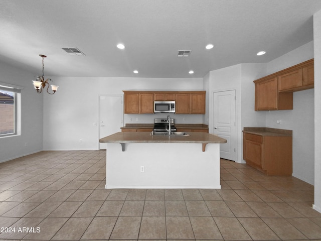 kitchen with light tile patterned flooring, a chandelier, a kitchen island with sink, appliances with stainless steel finishes, and a kitchen bar