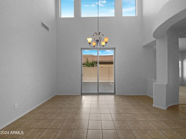 tiled spare room featuring a notable chandelier and a high ceiling