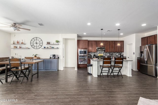 kitchen with a breakfast bar area, an island with sink, dark hardwood / wood-style floors, stainless steel appliances, and decorative light fixtures