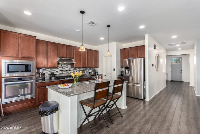 kitchen featuring dark hardwood / wood-style floors, an island with sink, stainless steel appliances, dark stone counters, and pendant lighting