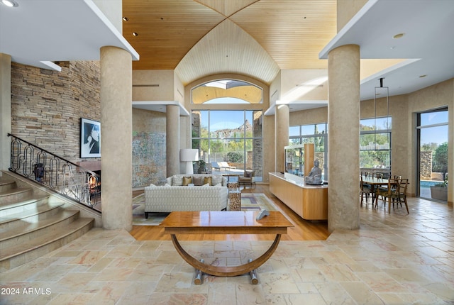 living room featuring light tile flooring, wood ceiling, ornate columns, and a towering ceiling