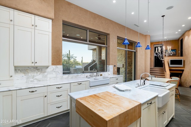 kitchen with an island with sink, dark parquet flooring, hanging light fixtures, sink, and white cabinetry