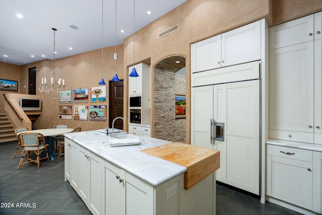 kitchen with paneled fridge, dark parquet flooring, hanging light fixtures, a kitchen island with sink, and white cabinetry